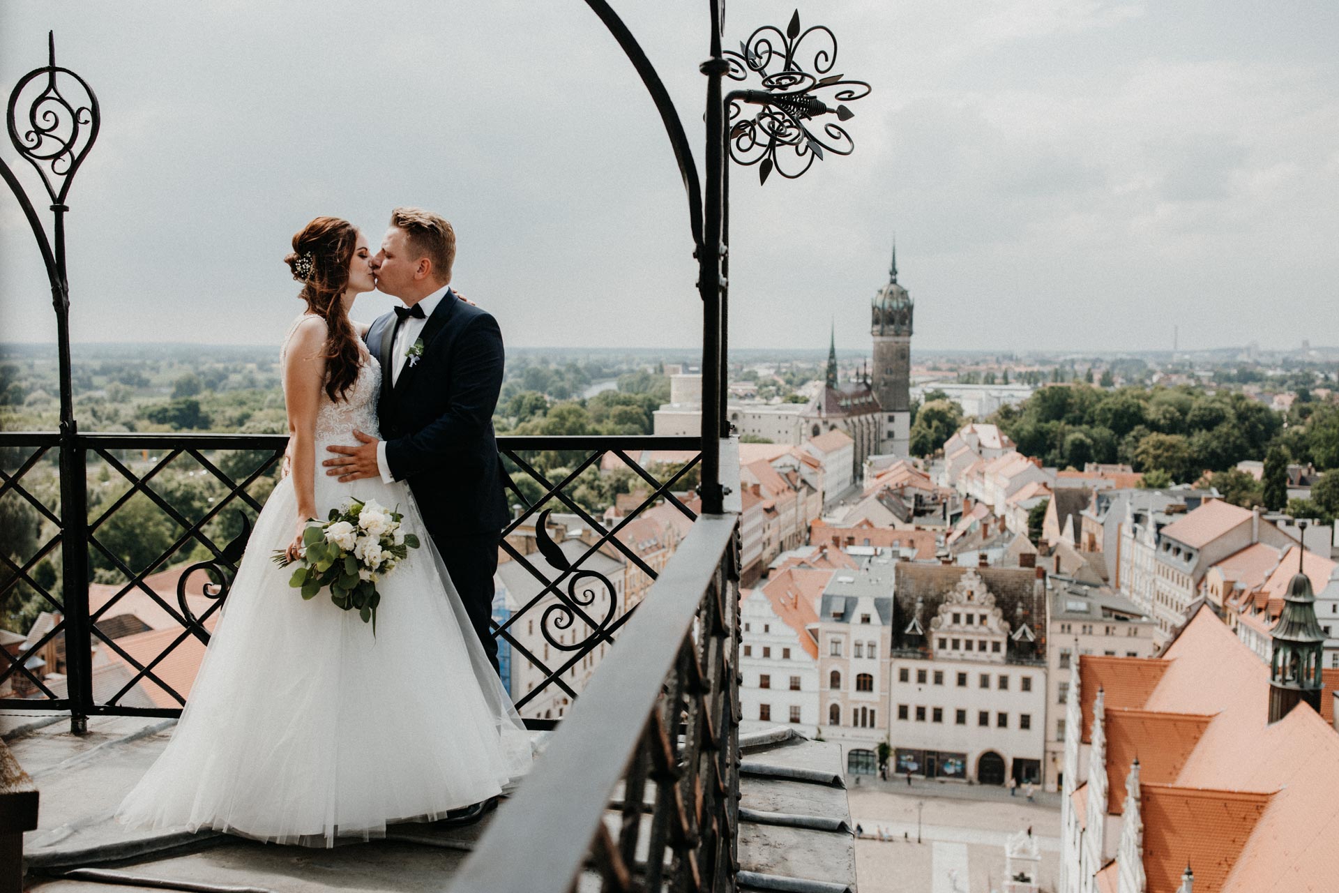 Hochzeitspaar auf einem Balkon mit Blick auf die Altstadt und Stadtkirche von Wittenberg